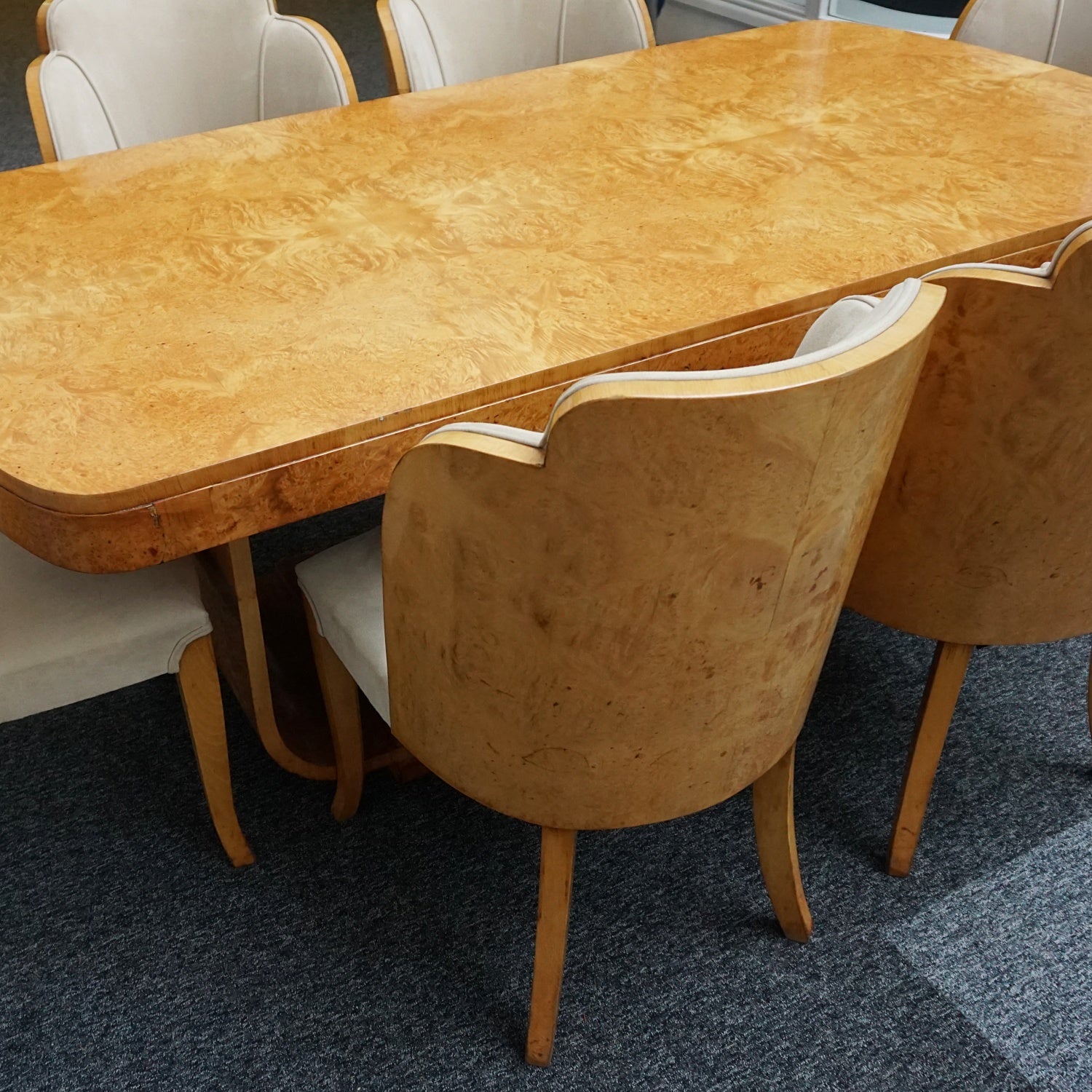 An art deco dining table with 6 chairs by Harry & Lou Epstein. The table top and cloud back armchairs are veneered in burr walnut. The chairs are upholstered in cream faux suede.