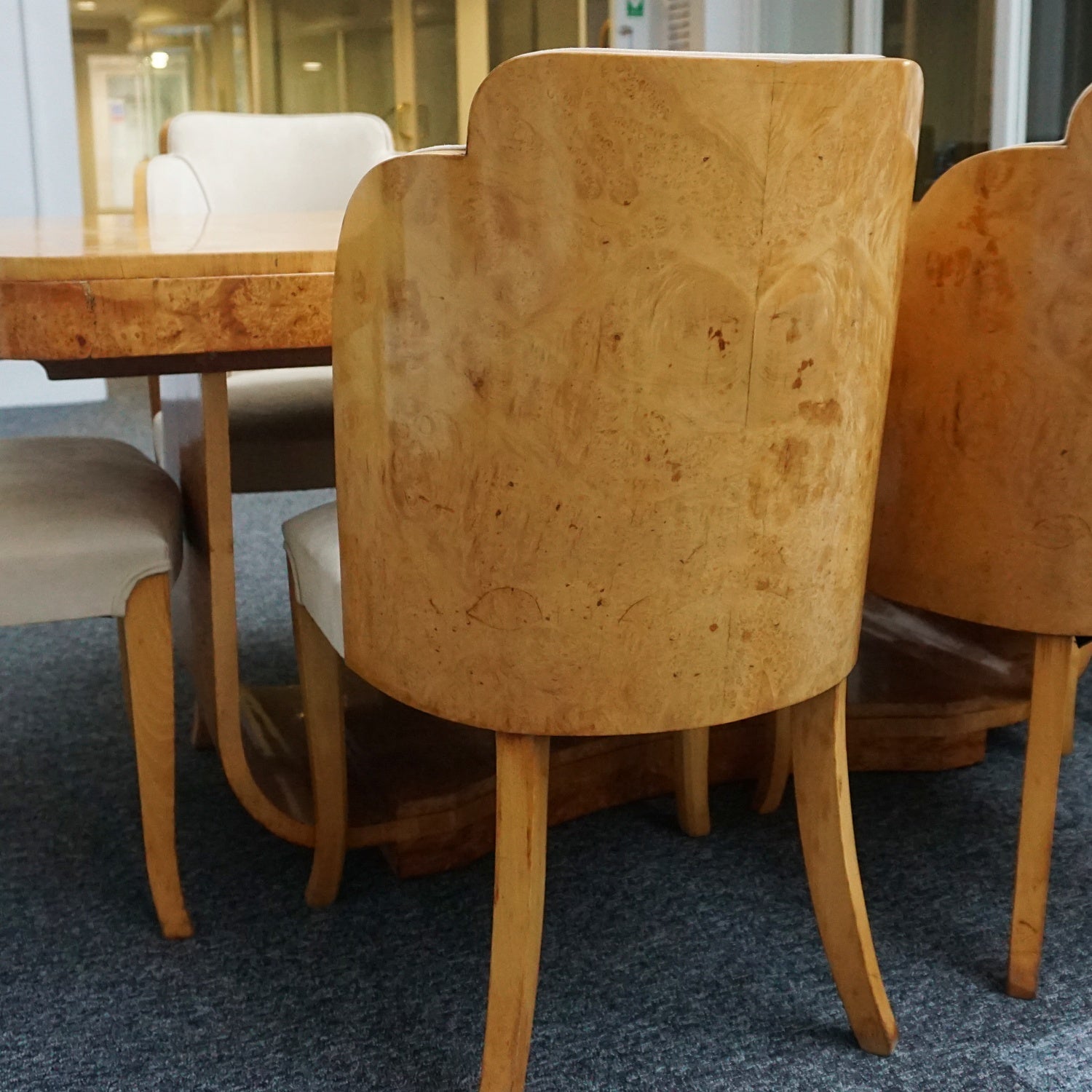 An art deco dining table with 6 chairs by Harry & Lou Epstein. The table top and cloud back armchairs are veneered in burr walnut. The chairs are upholstered in cream faux suede.