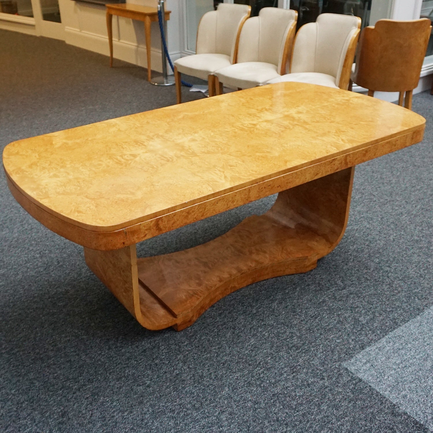 An art deco dining table with 6 chairs by Harry & Lou Epstein. The table top and cloud back armchairs are veneered in burr walnut. The chairs are upholstered in cream faux suede.