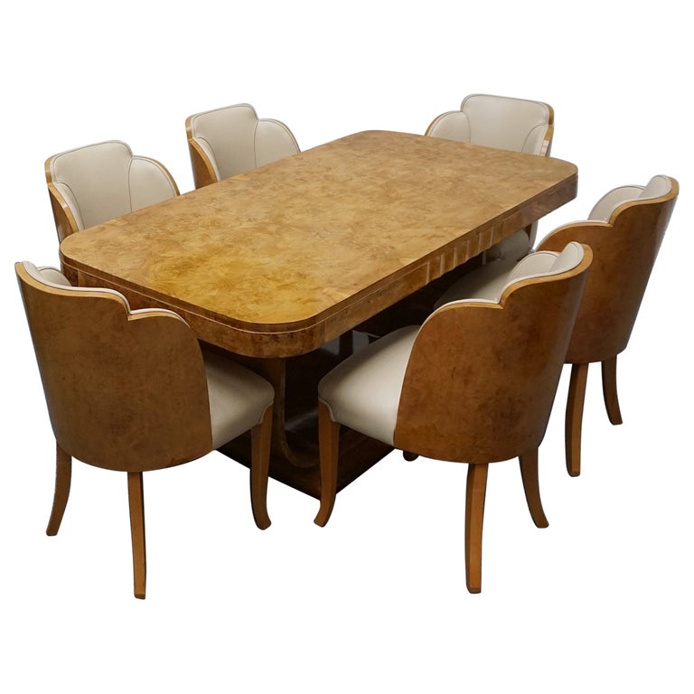An Art Deco dining table with six chairs by Harry & Lou Epstein. The table top is burr walnut veneered. The six matching cloud backed armchairs are upholstered in cream leather