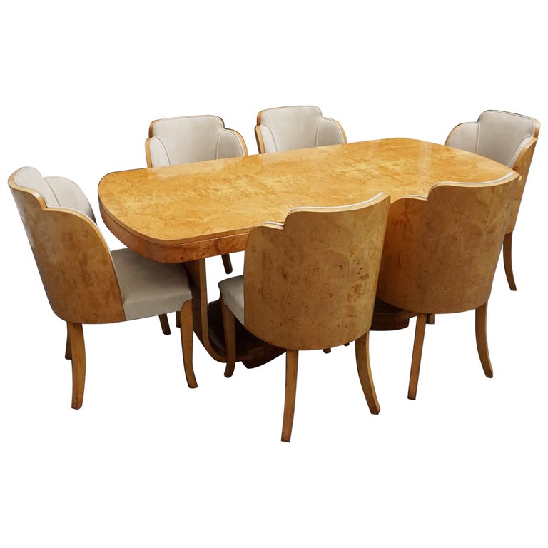 An art deco dining table with 6 chairs by Harry & Lou Epstein. The table top and cloud back armchairs are veneered in burr walnut. The chairs are upholstered in cream faux suede. 