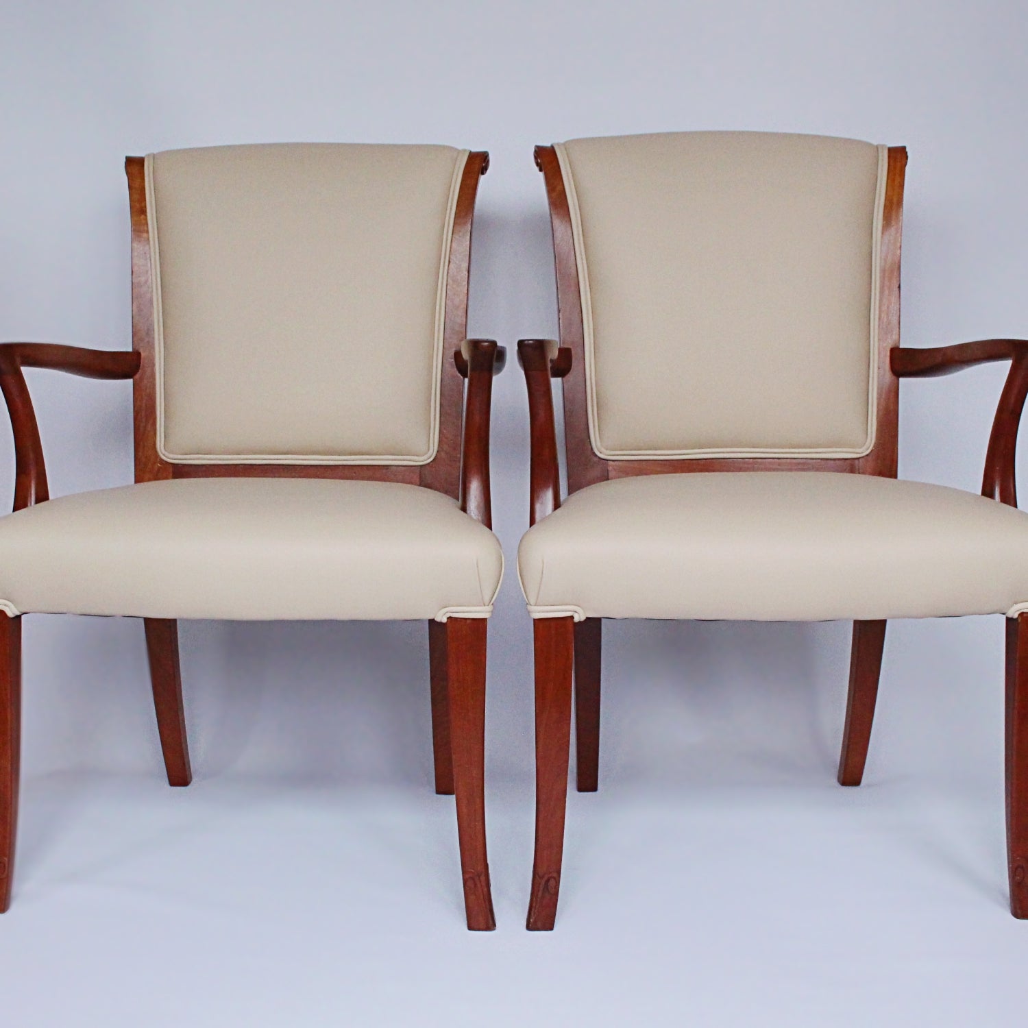 A pair of side chairs with walnut frames. Scrolled and carved detail to frames. Upholstered in cream leather. 