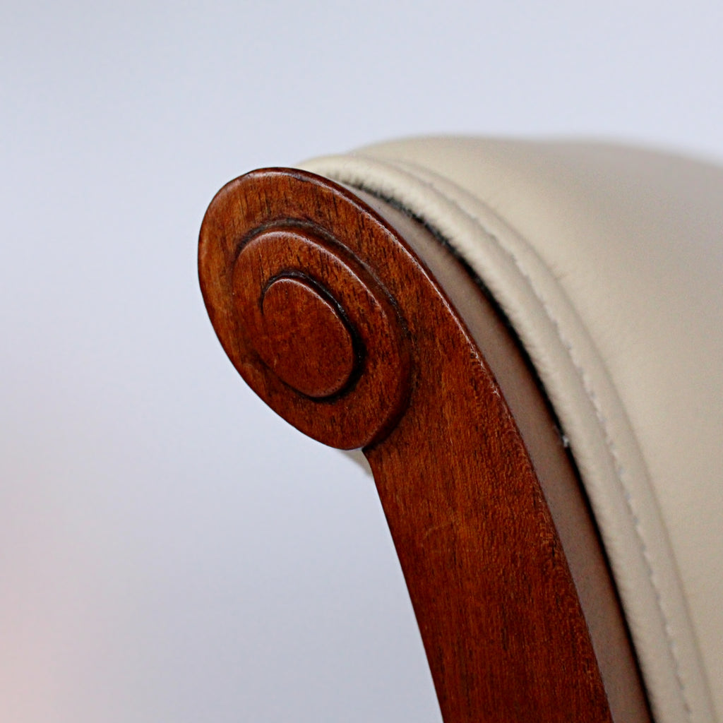 A pair of side chairs with walnut frames. Scrolled and carved detail to frames. Upholstered in cream leather. 