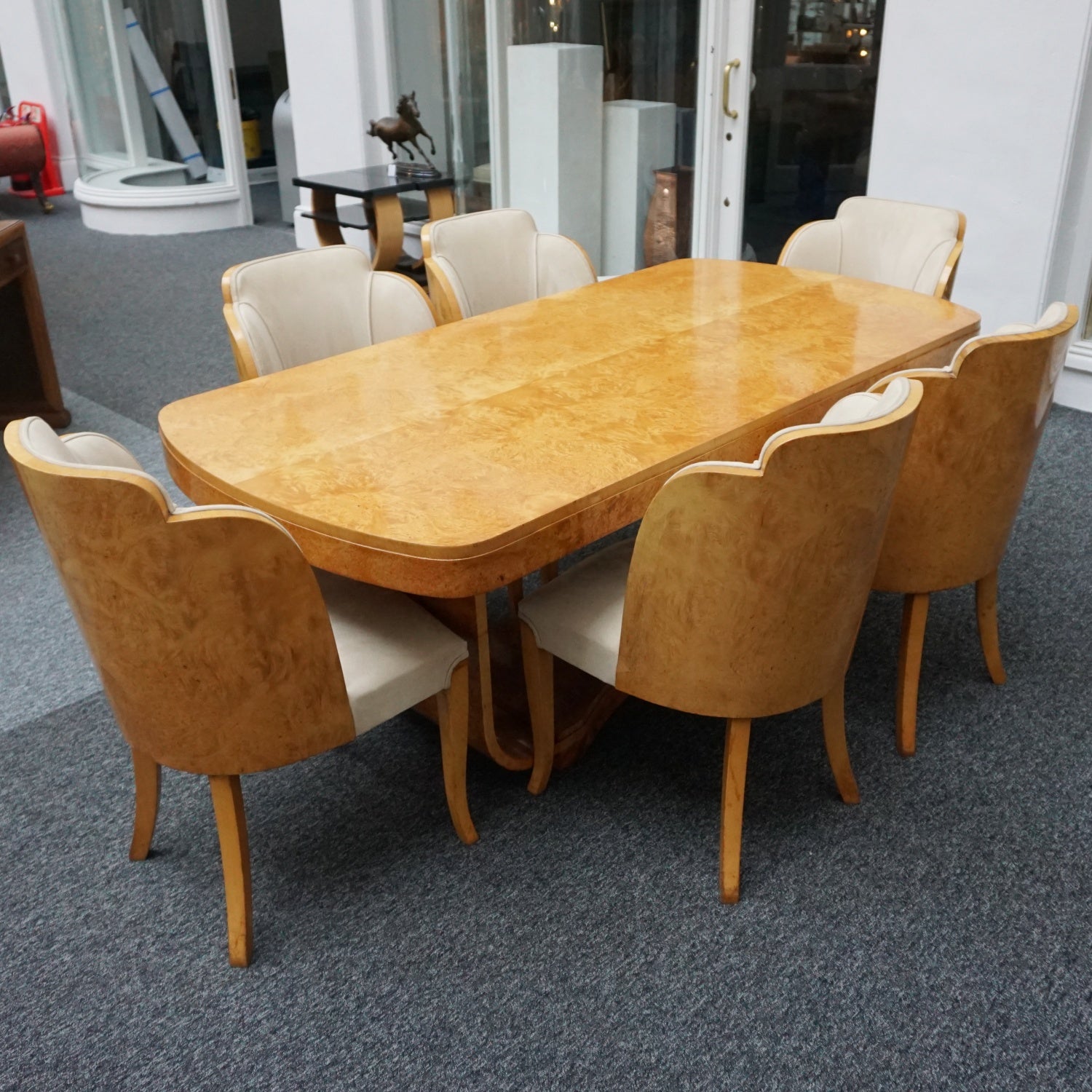 An art deco dining table with 6 chairs by Harry & Lou Epstein. The table top and cloud back armchairs are veneered in burr walnut. The chairs are upholstered in cream faux suede. 