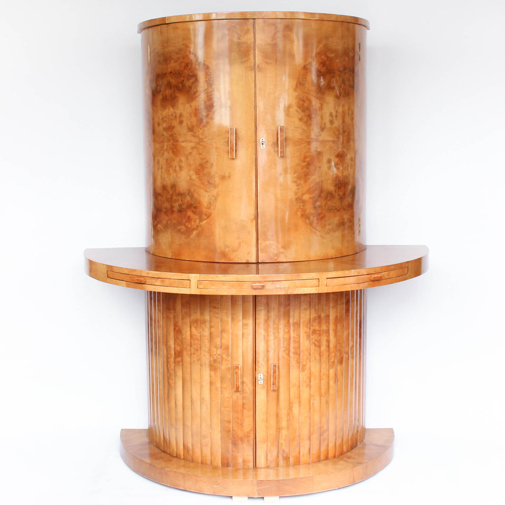 An Art Deco, demi-lune cocktail cabinet attributed to Harry & Lou Epstein. Mirrored, lit interior to top with glass shelves and mirrored slide tray. Lower, shelved cabinet with bottle holders. Burr walnut veneer at Jeroen Markies.