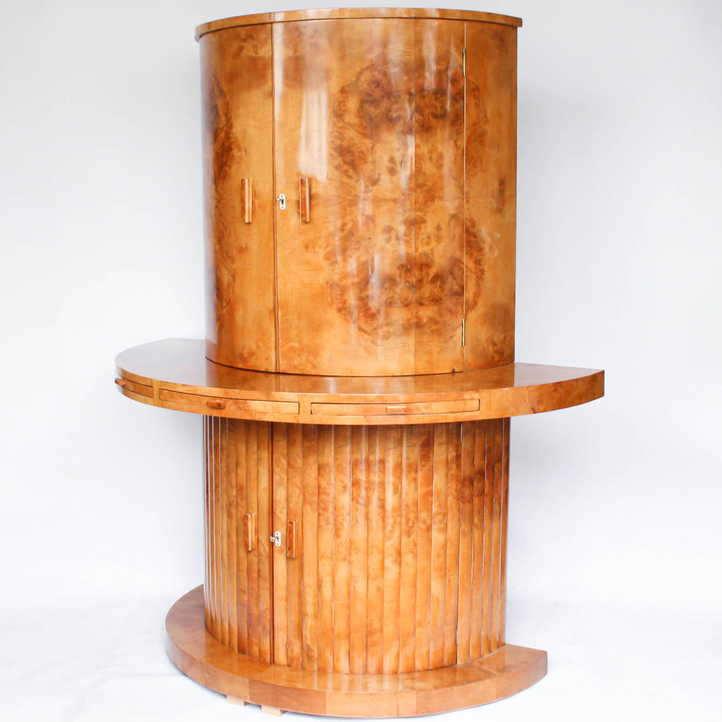 An Art Deco, demi-lune cocktail cabinet attributed to Harry & Lou Epstein. Mirrored, lit interior to top with glass shelves and mirrored slide tray. Lower, shelved cabinet with bottle holders. Burr walnut veneer at Jeroen Markies.
