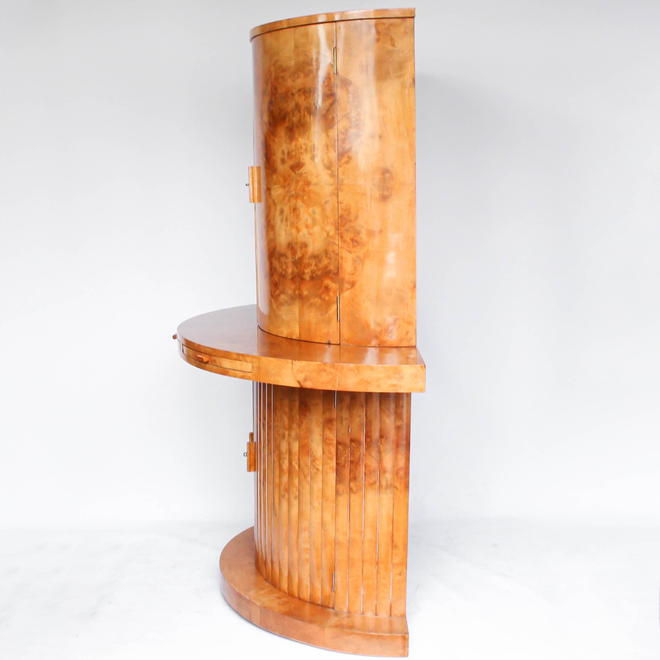 An Art Deco, demi-lune cocktail cabinet attributed to Harry & Lou Epstein. Mirrored, lit interior to top with glass shelves and mirrored slide tray. Lower, shelved cabinet with bottle holders. Burr walnut veneer at Jeroen Markies.