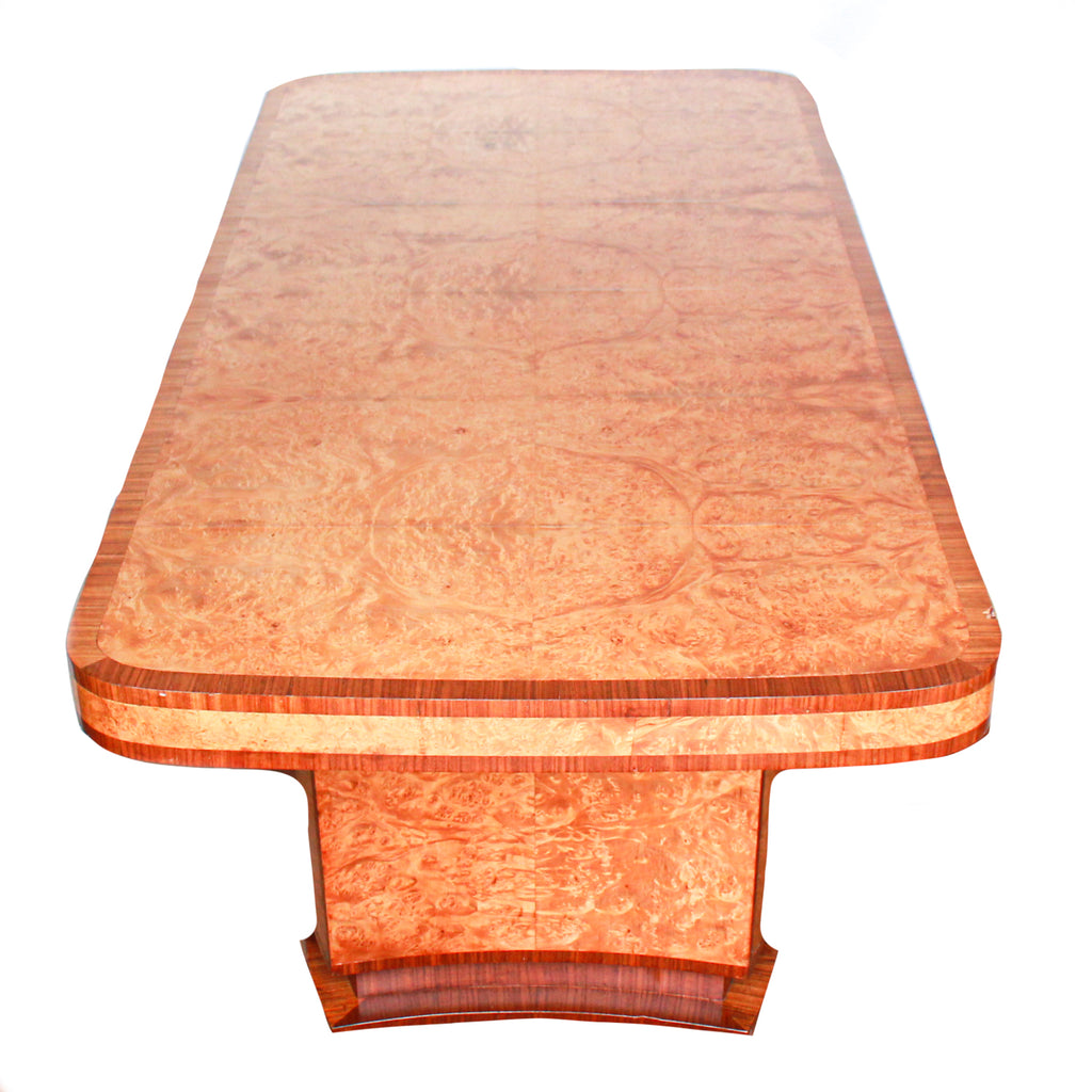 An Art Deco dining table and six chairs. Serpentine edged, burr walnut table set over pedestal legs in straight grain walnut with burr walnut reeded detail. Cloud back chairs upholstered in cream leather.