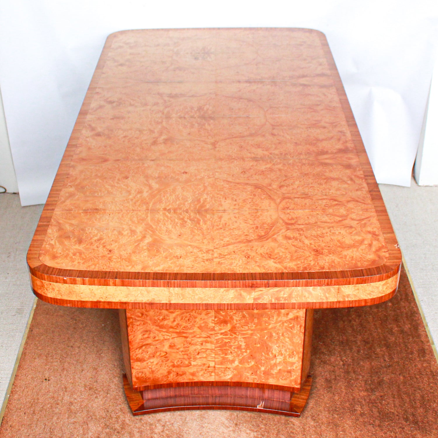 An Art Deco dining table and six chairs. Serpentine edged, burr walnut table set over pedestal legs in straight grain walnut with burr walnut reeded detail. Cloud back chairs upholstered in cream leather.