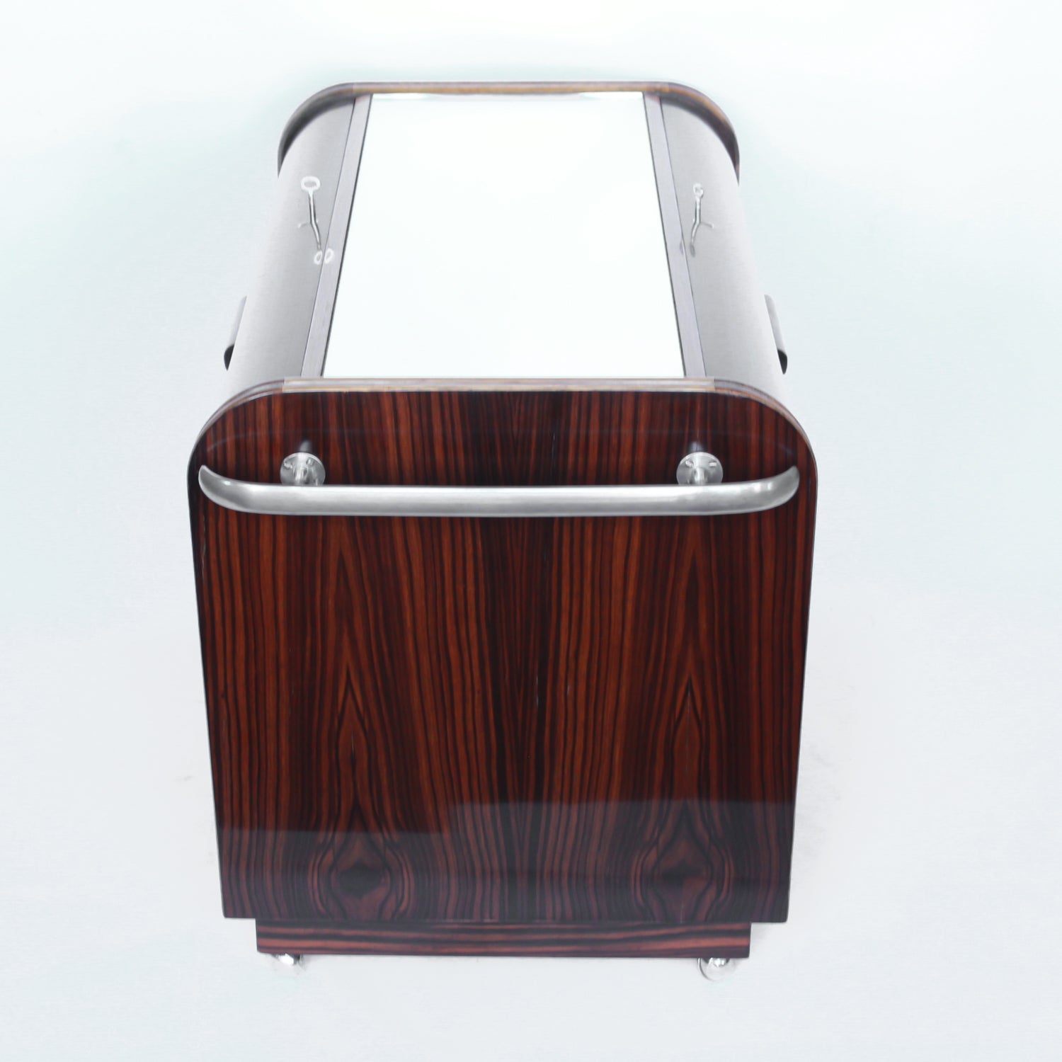 An Art Deco serving/drinks trolley with mirrored top. Double ice-box to one side with drinks cabinet to opposite side, including lower compartment for glasses. Macassar ebony throughout with walnut banding. Original chrome handle and rolling castors.