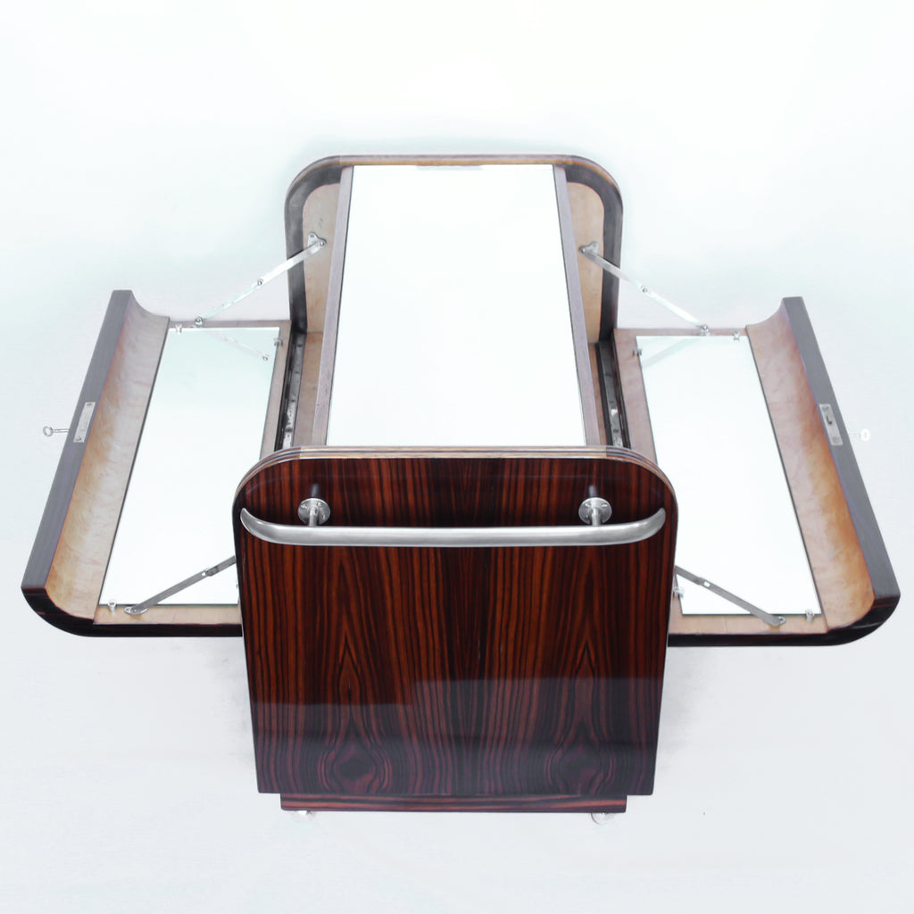 An Art Deco serving/drinks trolley with mirrored top. Double ice-box to one side with drinks cabinet to opposite side, including lower compartment for glasses. Macassar ebony throughout with walnut banding. Original chrome handle and rolling castors.