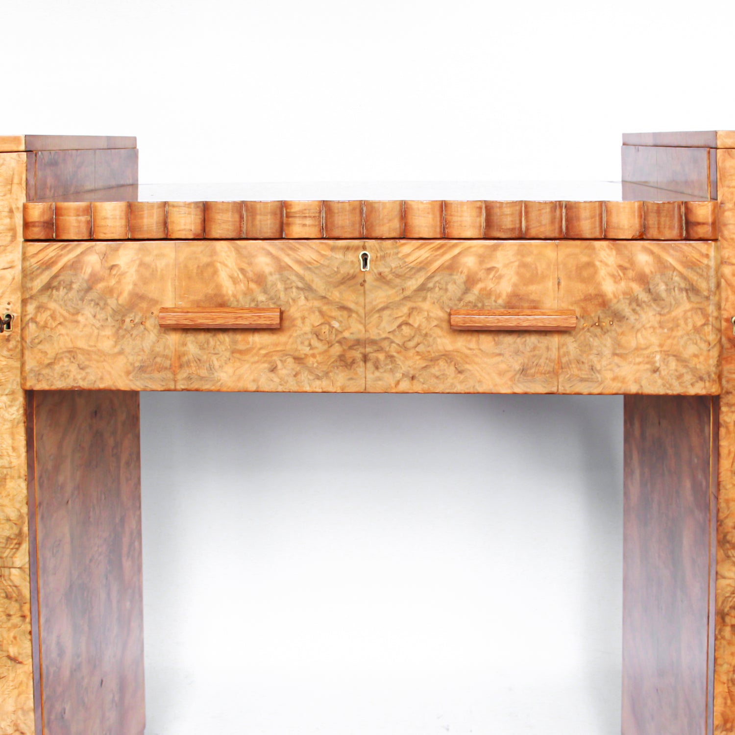 An Art Deco console sideboard by Hille. Burr walnut veneer throughout. Scallop-edged detail to front with integral drawer. Shelved cabinets to either side.