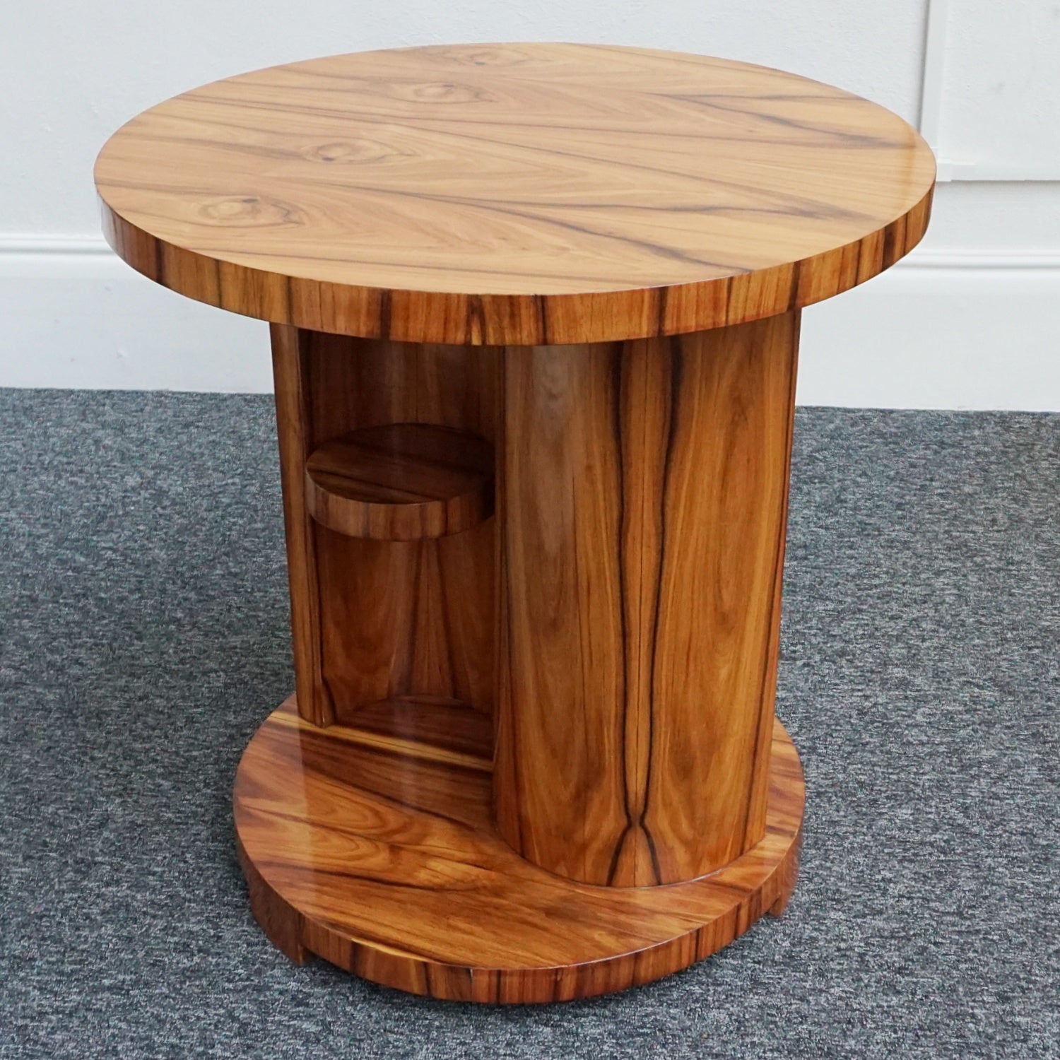 An Art Deco style centre table with a curved central column with hidden shelf to either side set over a circular base made from burr walnut veneer